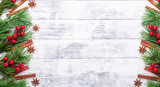 Fototapeta Nowy Jork - Christmas background with fir tree, spice and red holly on woodeen table. Horizontal banner. Top view Copy space - Image