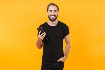 Image of happy man wearing black t-shirt smiling and holding smartphone