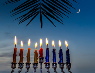 Glitter lights of candles are traditional symbols for Jewish Hanukkah Holiday of light.  Selective focus on candles with blurred sky background