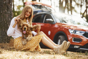 Leaning on the tree. Woman with her dog outdoors in the forest against automobile have good time