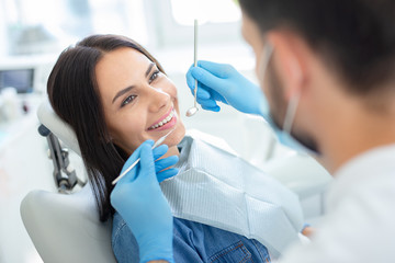 smiling happy client in dental chair with doctor looking her with instruments