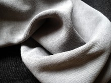 Close-up And Texture Of A Knitted Fabric Or Scarf Of Gray Color, Slightly Folded Round And Wrinkled. A Play Of Light And Shadow In Natural Daylight. Soft, Warm Cotton Or Natural Wool.