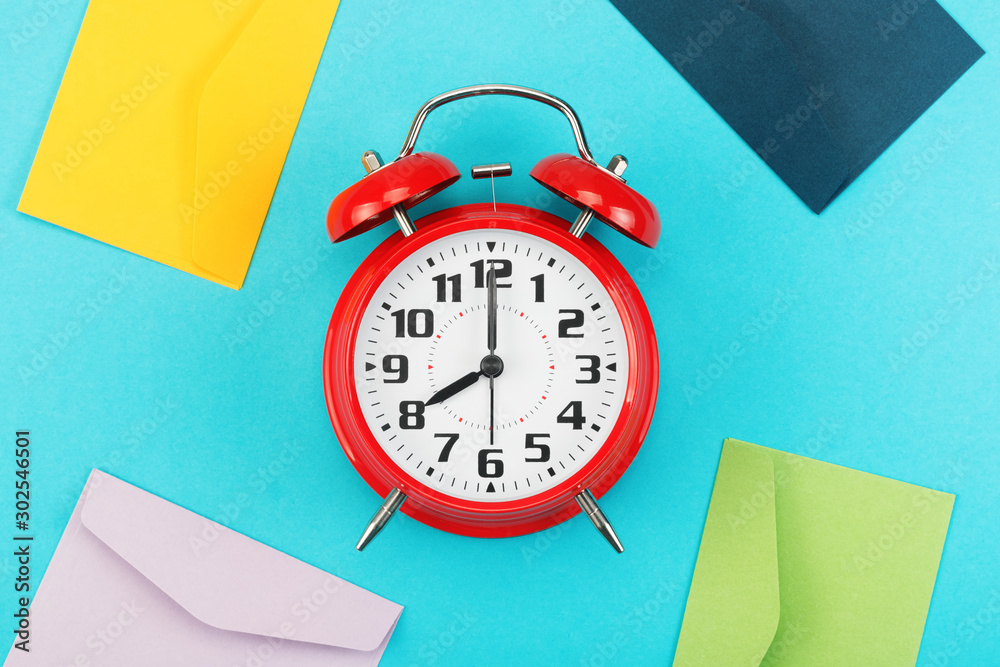 Colorful envelopes around the red alarm clock on a blue background. The ...