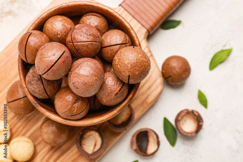 Bowl with macadamia nuts on white background
