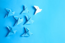White Origami Bird Among Blue Ones On Color Background. Concept Of Uniqueness