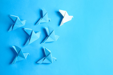 White origami bird among blue ones on color background. Concept of uniqueness