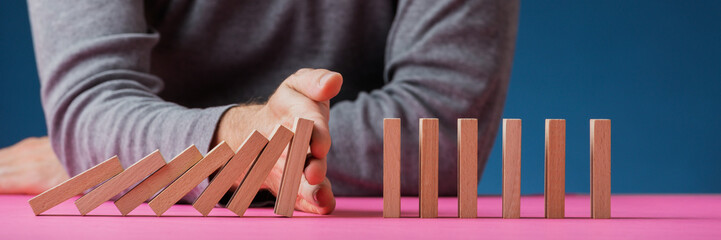 Man stopping dominos on pink surface from collapsing