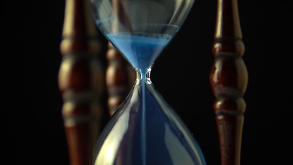 Wall Mural - Hourglass clock time concept. Old vintage wood frame blue sand clock countdown on dark background. Close up.