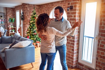 Middle age beautiful couple smiling happy and confident. Standing and dancing around christmas tree at home