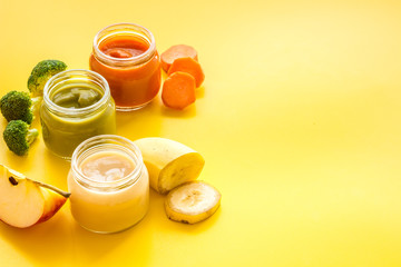 Baby food. Colorful puree in glass jars near vegetables and fruits on yellow background space for text