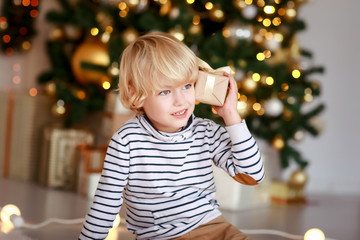 A blond-haired boy against the background of luminous light bulbs is trying to guess which gift is inside the box.