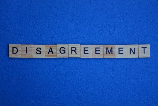 the word disagreement of brown wooden letters lies on a blue table