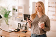 © JustLife - Young businesswoman in office. Beautiful woman drinking coffee and typing message.