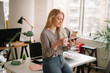 © JustLife - Young woman in office. Beautiful woman on coffee break using phone.