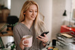 © JustLife - Close up of businesswoman in office drinking coffee and using phone.
