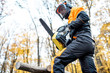 Professional lumberjack in protective workwear working with a chainsaw in the forest. Woodcutter makes a logging outdoors
