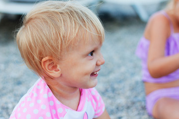 Wall Mural - Beautiful smiling blond toddler girl wearing pink swimsuit sitting on the beach