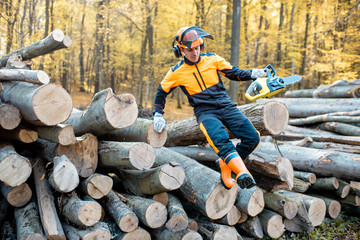 Canvas Print - Professional lumberjack in protective workwear jumping with a chainsaw from a pile of logs in the forest