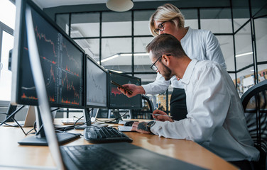 Analyzing information together. Two stockbrokers in formal clothes works in the office with financial market