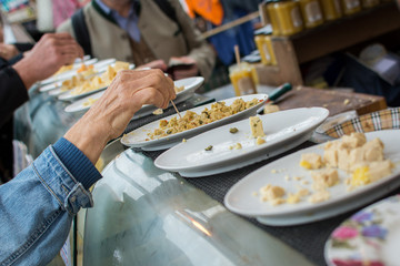 Samples of various cheeses on plates, hand with toothpick picking up a piece of cheese to taste try at a food stand