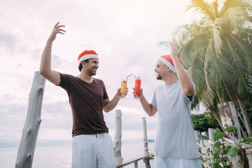 Friends with cocktails in Christmas caps on the ocean on a tropical island