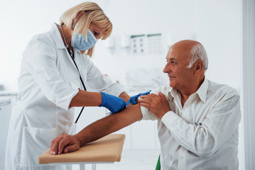 Female doctor injecting senior male patient with syringe in the clinic