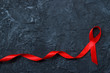 Red ribbon as symbol of aids awareness on black background. Medical care campaign