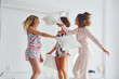 © standret - Pillow fight. Happy female friends having good time at pajama party in the bedroom