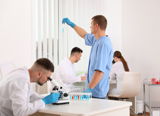 Poster - Scientist using microscope at table and colleagues in laboratory. Medical research