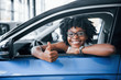 © standret - Shows thumb up. Young african american woman sits inside of new modern car