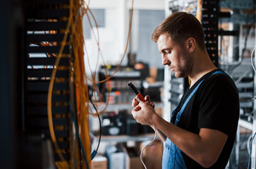 Wall Mural - Young man in uniform with measuring device works with internet equipment and wires in server room
