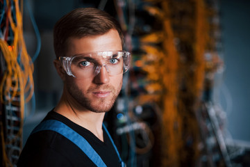 Wall Mural - Young man in uniform works with internet equipment and wires in server room