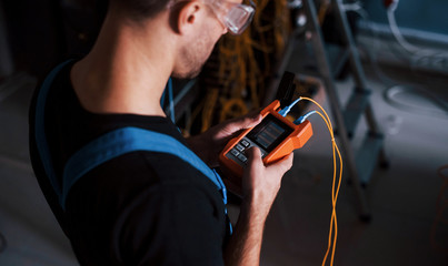 Wall Mural - Young man in uniform with measuring device works with internet equipment and wires in server room