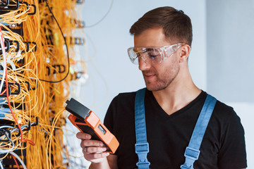 Wall Mural - Young man in protective glasses works with internet equipment and wires in server room