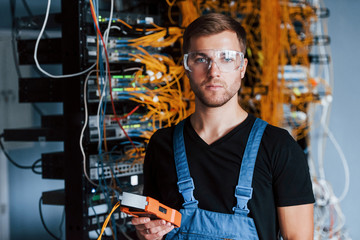 Wall Mural - Young man in protective glasses works with internet equipment and wires in server room