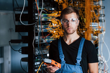 Wall Mural - Young man in protective glasses works with internet equipment and wires in server room
