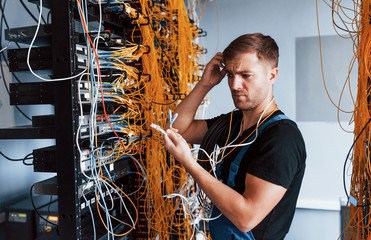 Wall Mural - Young man in uniform feels confused and looking for a solution with internet equipment and wires in server room