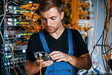 Wall Mural - Young man in uniform have a job with internet equipment and wires in server room