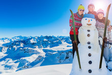 Happy Family Enjoying Winter With Snowman Vacations In Mountains, Playing With Snow And Sun In High Mountains. Winter Holidays.