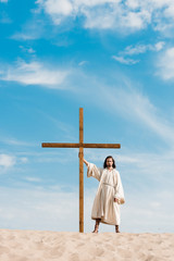 Wall Mural - bearded man standing with wooden cross in desert on sand