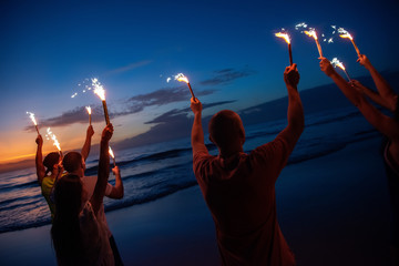 Canvas Print - Happy friends at sunset beach party with fireworks