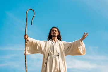 Poster - jesus with outstretched hands holding wooden cane against blue sky