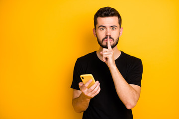 Sticker - Censorship no telling secret concept. Serious guy blogger hold use cellphone search private fake news show mute quiet sign index finger wear black t-shirt isolated yellow color background