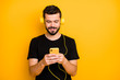 © deagreez - Portrait of positive cheerful guy listen music use yellow headset search song on his cellphone want choose sound track wear casual style clothing isolated over bright color background