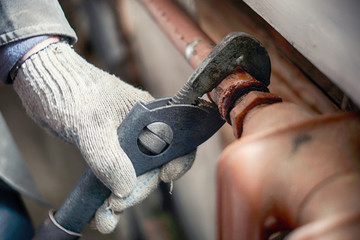  A man in working gloves with a pipe spanner unscrews an old cast-iron heating system battery