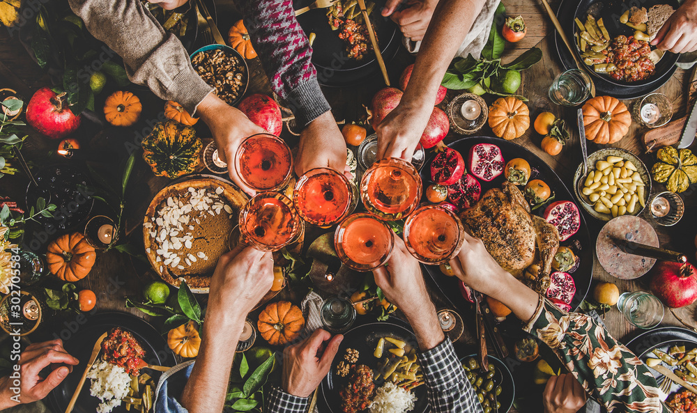 Family celebrating Thanksgiving day. Flat-lay of feasting peoples hands clinking glasses with rose wine over Friendsgiving table with traditional Fall food, roasted turkey, pumpkin pie, top view - obrazy, fototapety, plakaty 