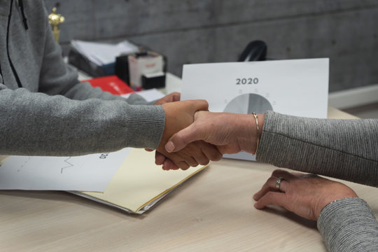 Two women shaking hands closing a deal with background year graphics