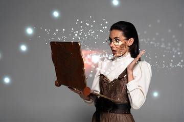 Wall Mural - shocked steampunk woman in glasses using vintage laptop with glowing illustration isolated on grey