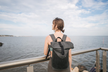 girl with a backpack travels standing by the sea