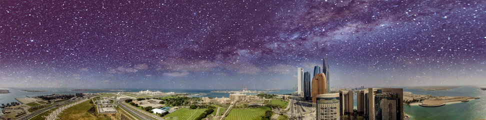 Amazing panoramic aerial view of Abu Dhabi skyscrapers from Corniche Road on a starry night with milky way